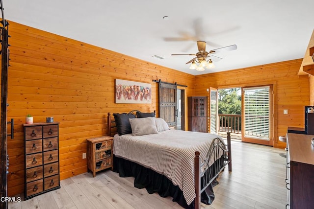 bedroom featuring light hardwood / wood-style floors, wood walls, access to outside, ceiling fan, and a barn door