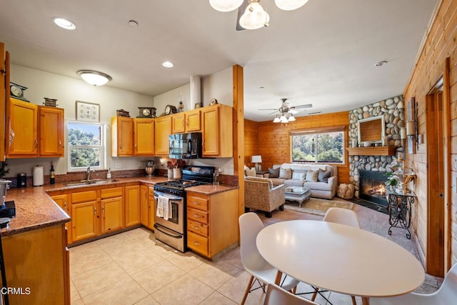 kitchen with dark stone counters, a fireplace, ceiling fan, sink, and gas range