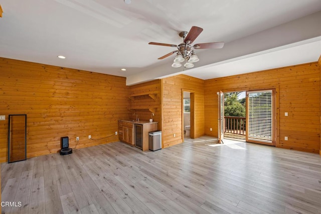 unfurnished living room with ceiling fan, light hardwood / wood-style flooring, and wood walls