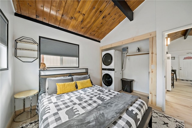 bedroom with light wood-type flooring, lofted ceiling with beams, wooden ceiling, and stacked washing maching and dryer