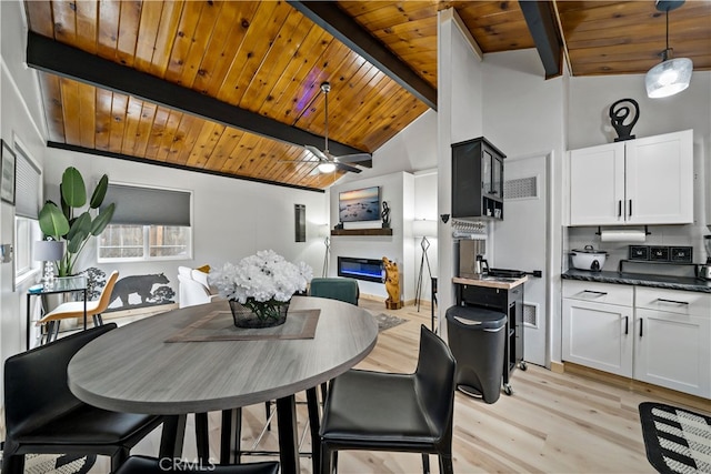 dining room with ceiling fan, beam ceiling, wooden ceiling, light wood-type flooring, and a large fireplace