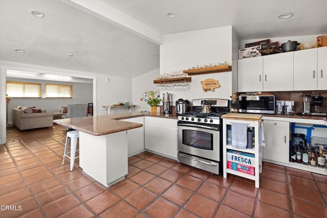 kitchen with a kitchen breakfast bar, dark tile patterned flooring, white cabinets, kitchen peninsula, and stainless steel appliances