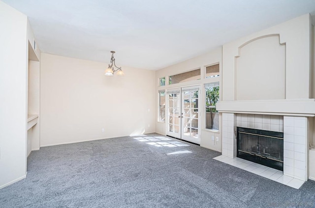 unfurnished living room with light colored carpet, an inviting chandelier, and a tiled fireplace