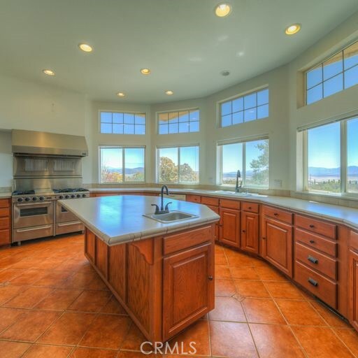 kitchen featuring ventilation hood, stainless steel range, an island with sink, and sink