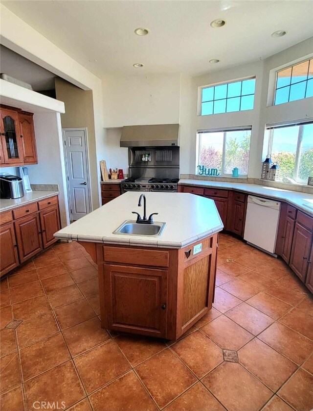 kitchen featuring dark tile patterned flooring, sink, a center island with sink, wall chimney range hood, and dishwasher