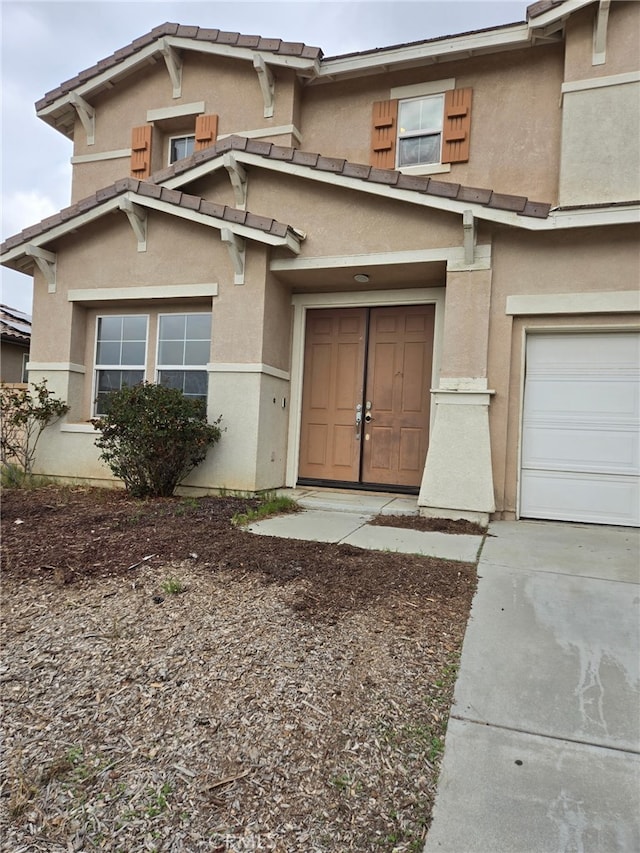 entrance to property featuring a tile roof, an attached garage, and stucco siding