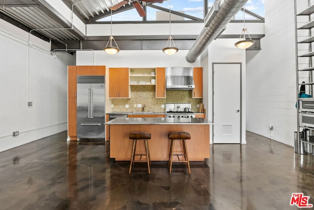 kitchen featuring range, a towering ceiling, a kitchen breakfast bar, stainless steel built in fridge, and wall chimney exhaust hood