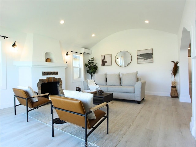 living room with light hardwood / wood-style flooring, vaulted ceiling, a fireplace, and a wall mounted air conditioner