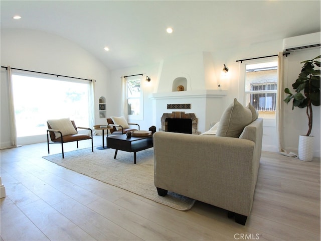 living room with light wood-type flooring, a fireplace, an AC wall unit, and lofted ceiling