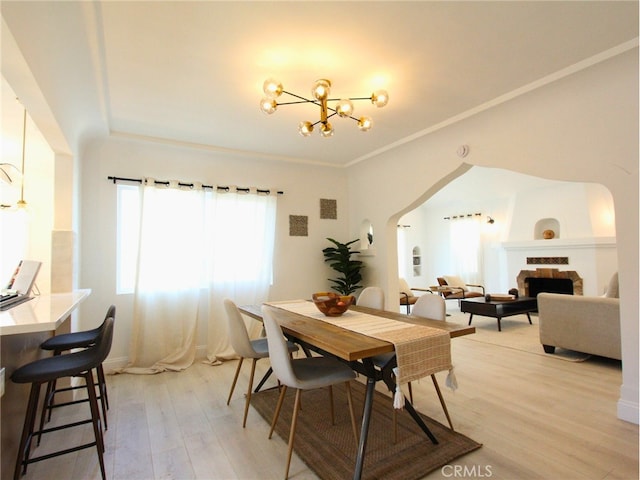 dining room with a notable chandelier, light wood-type flooring, crown molding, and a large fireplace