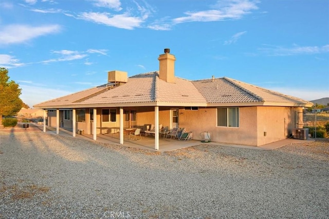 rear view of property with central air condition unit, a patio area, a chimney, a tile roof, and stucco siding
