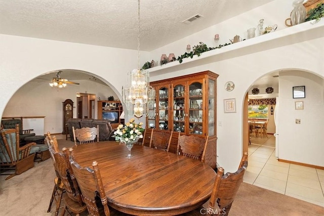 dining room with visible vents, light tile patterned floors, arched walkways, ceiling fan with notable chandelier, and light colored carpet