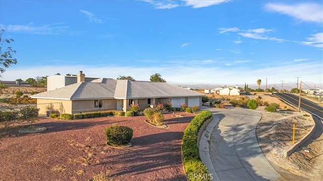 ranch-style house featuring driveway, stucco siding, a chimney, and an attached garage