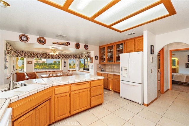 kitchen with ceiling fan, sink, backsplash, tile countertops, and white fridge with ice dispenser