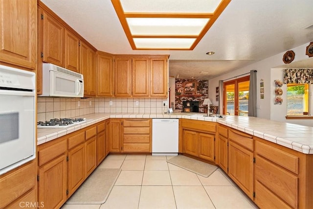 kitchen with a fireplace, white appliances, light tile patterned floors, a peninsula, and decorative backsplash