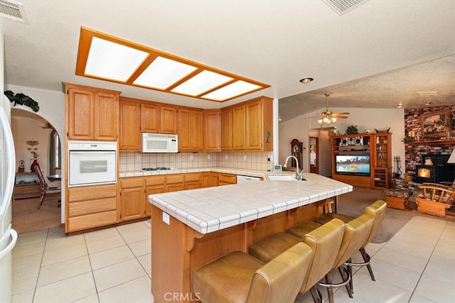 kitchen with kitchen peninsula, white appliances, tile countertops, light tile patterned floors, and ceiling fan