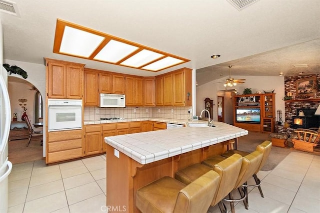 kitchen featuring tile countertops, light tile patterned floors, white appliances, visible vents, and a sink