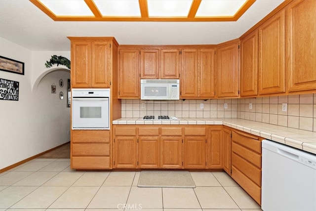 kitchen with light tile patterned floors, tile countertops, tasteful backsplash, and white appliances