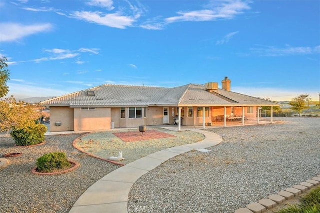 rear view of house with a patio area, stucco siding, a tiled roof, and a chimney