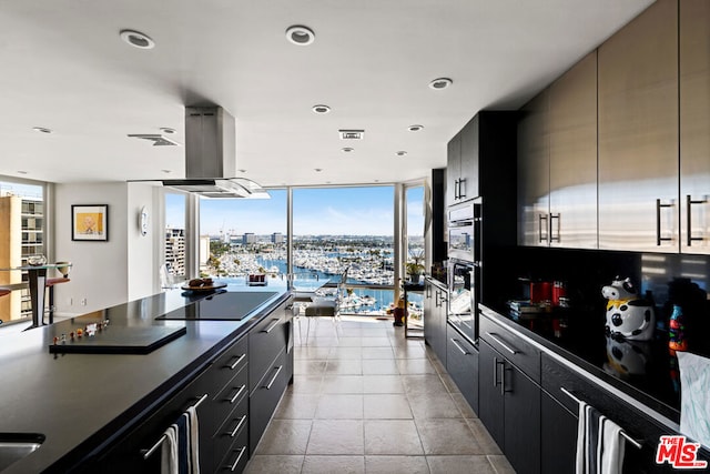 kitchen featuring a water view, light tile patterned floors, expansive windows, island exhaust hood, and black electric stovetop