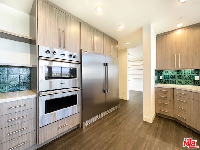 kitchen featuring backsplash, dark wood-type flooring, light brown cabinetry, appliances with stainless steel finishes, and light stone counters