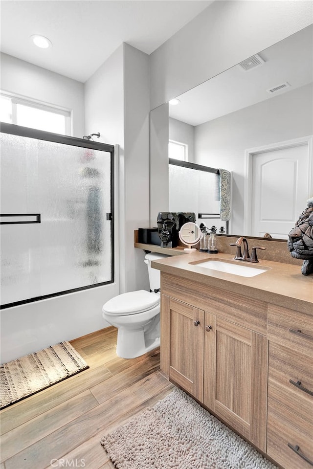 full bathroom featuring bath / shower combo with glass door, hardwood / wood-style flooring, vanity, and toilet