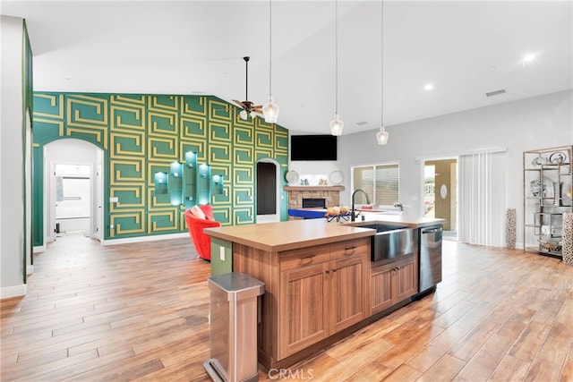 kitchen with pendant lighting, light wood-type flooring, sink, a center island with sink, and stainless steel dishwasher