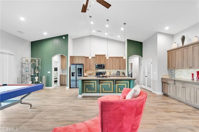 kitchen featuring ceiling fan, a kitchen island with sink, stainless steel appliances, and high vaulted ceiling