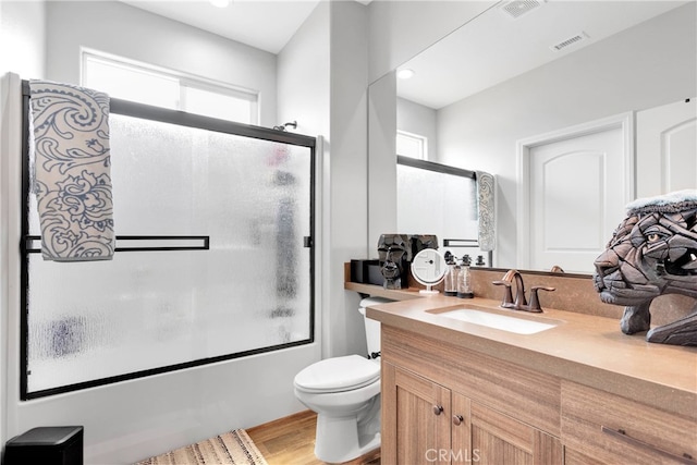 full bathroom with bath / shower combo with glass door, hardwood / wood-style flooring, vanity, and toilet