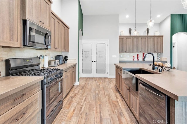 kitchen with sink, decorative light fixtures, a center island with sink, light hardwood / wood-style flooring, and stainless steel appliances