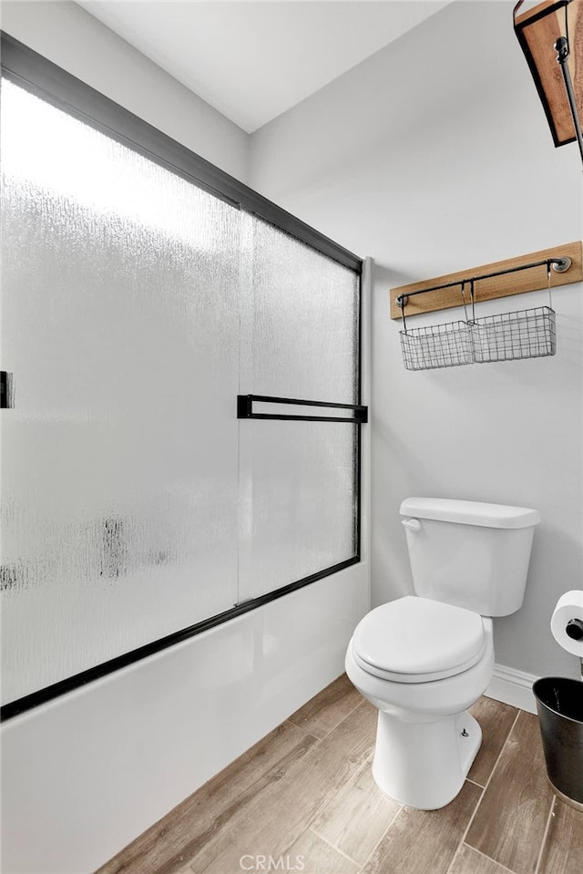 bathroom featuring wood-type flooring, combined bath / shower with glass door, and toilet