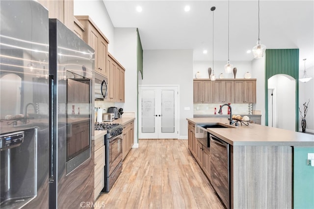 kitchen featuring appliances with stainless steel finishes, tasteful backsplash, pendant lighting, light hardwood / wood-style flooring, and a center island with sink