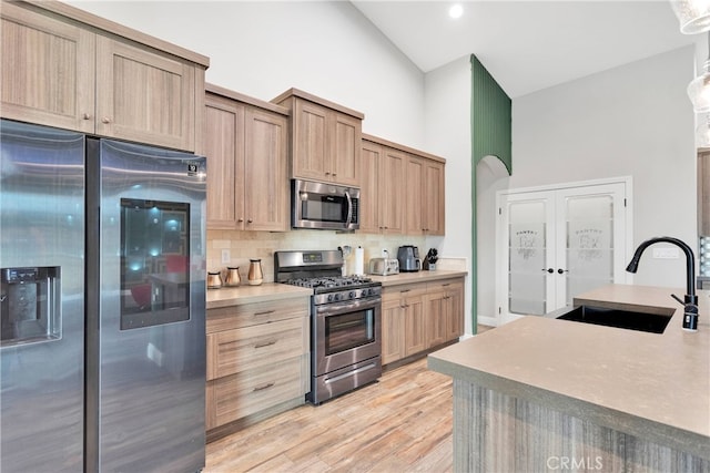 kitchen with light wood-type flooring, sink, high vaulted ceiling, decorative backsplash, and appliances with stainless steel finishes