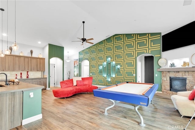 living room with lofted ceiling, a stone fireplace, ceiling fan with notable chandelier, light hardwood / wood-style flooring, and billiards