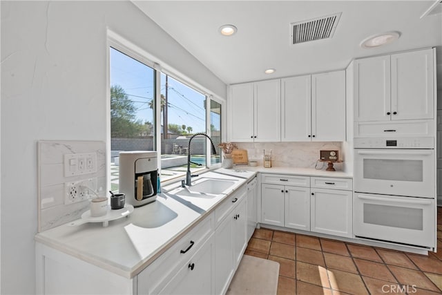 kitchen with tasteful backsplash, white double oven, sink, and white cabinets