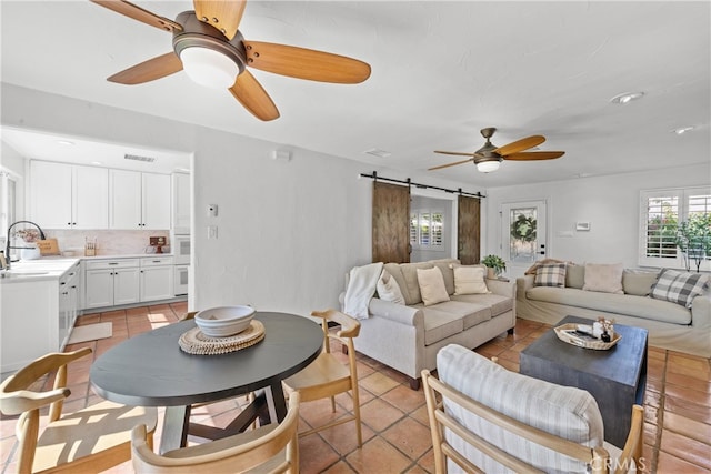 living room with a barn door, light tile patterned floors, sink, and ceiling fan