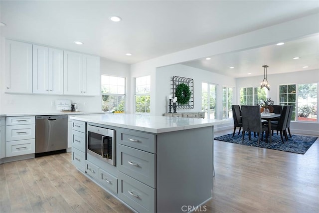 kitchen with light hardwood / wood-style flooring, white cabinetry, appliances with stainless steel finishes, and hanging light fixtures