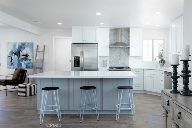 kitchen featuring wall chimney exhaust hood, stainless steel appliances, white cabinets, and a center island