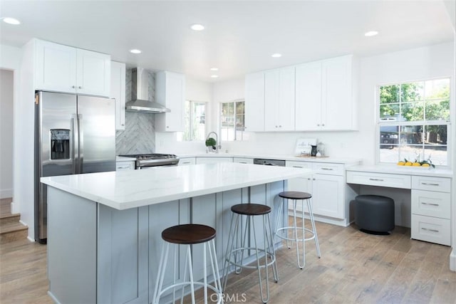 kitchen featuring light hardwood / wood-style floors, white cabinets, wall chimney range hood, and plenty of natural light