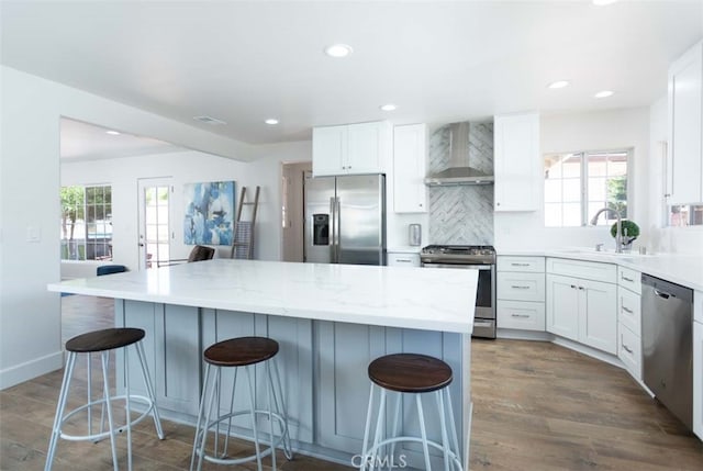 kitchen with a breakfast bar, a wealth of natural light, white cabinets, wall chimney exhaust hood, and stainless steel appliances