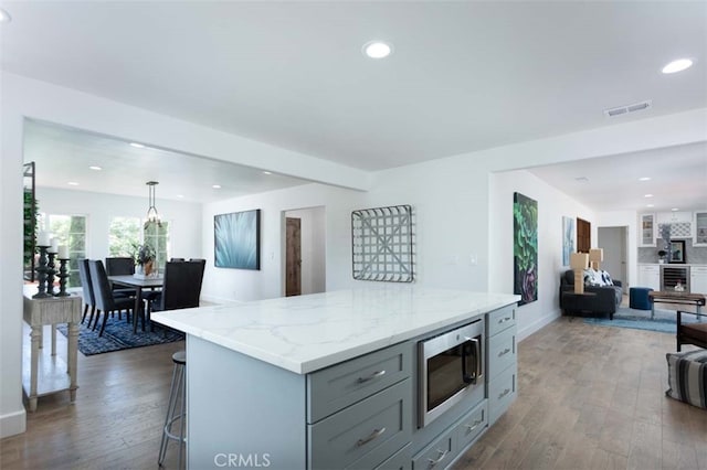 kitchen featuring stainless steel microwave, a kitchen island, a breakfast bar area, dark hardwood / wood-style flooring, and decorative light fixtures