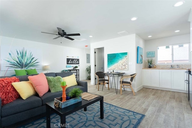 living room with ceiling fan, electric panel, light wood-type flooring, and sink