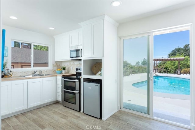 kitchen with appliances with stainless steel finishes, light wood-type flooring, white cabinetry, and sink