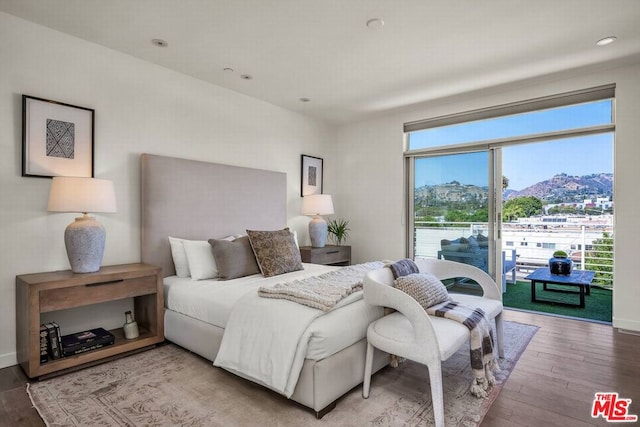 bedroom with multiple windows, wood-type flooring, a mountain view, and access to exterior