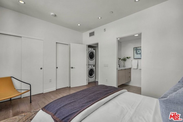 bedroom with light wood-type flooring, connected bathroom, and stacked washer / dryer