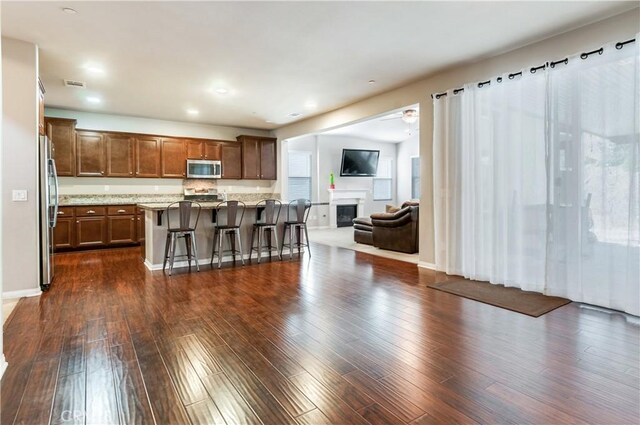 kitchen with dark wood-type flooring, light stone counters, a breakfast bar, a kitchen island, and stainless steel appliances