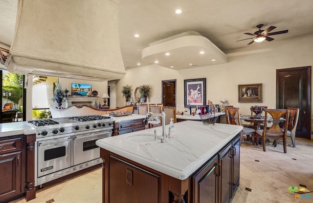 kitchen featuring light stone counters, range with two ovens, ceiling fan, a kitchen island with sink, and sink