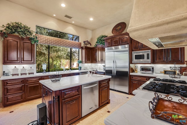 kitchen featuring built in appliances, a kitchen island, backsplash, exhaust hood, and light stone countertops