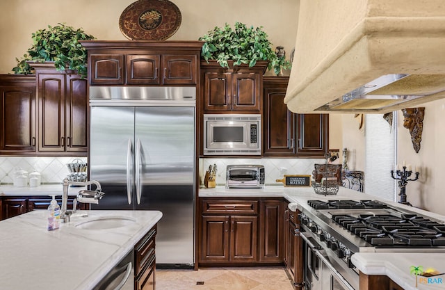 kitchen with tasteful backsplash, built in appliances, exhaust hood, dark brown cabinetry, and sink