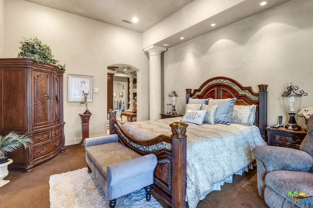 bedroom featuring a high ceiling, decorative columns, and dark carpet